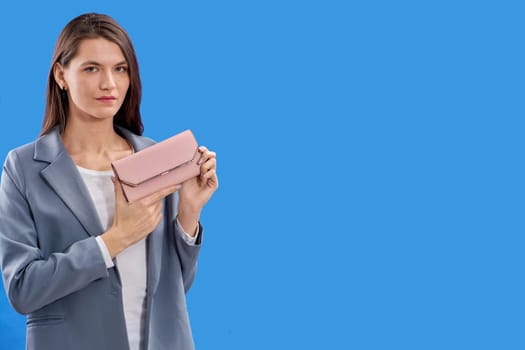 A beautiful young woman is holding a pink purse on a blue background, copy space. High quality photo