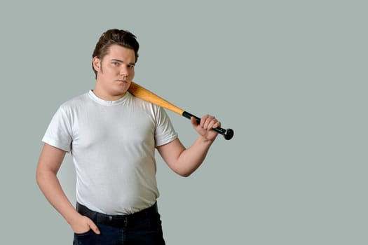 A stylish man holds a bat on his shoulder on a gray isolated background. High quality photo