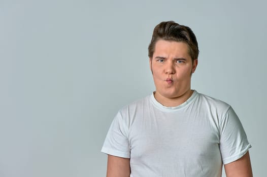 a man puffing out his cheeks with a funny face on a gray background, emotions. High quality photo