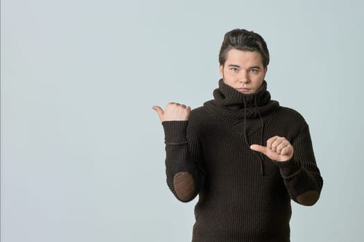 a man in a brown sweater and a bright color points to something and perfectly, showing an empty space with his thumb, shows everything on a light background, copy space. High quality photo