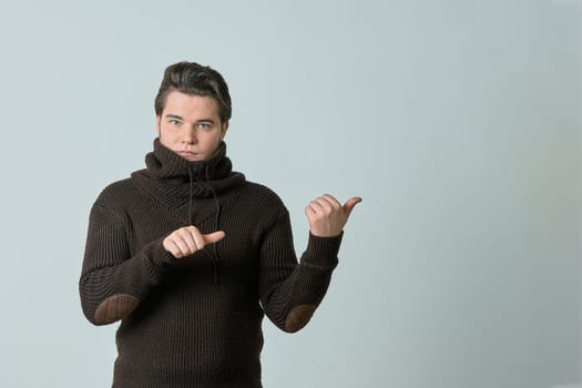 a man in a brown sweater and a bright color points to something and perfectly, showing an empty space with his thumb, shows everything on a light background, copy space. High quality photo