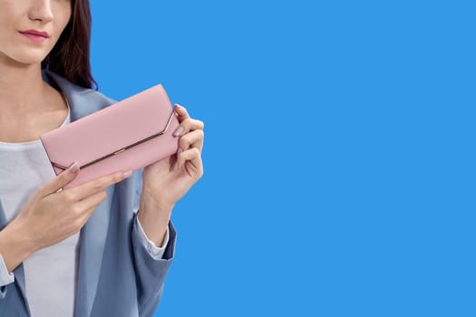A beautiful young woman is holding a pink purse on a blue background, copy space. High quality photo