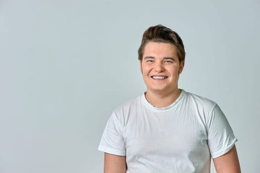 A man in a white T-shirt on a gray background smiles. High quality photo
