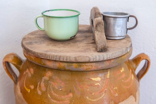 Large earthenware jar with lid and cups for drinking water. Old Cottage kitchen concept