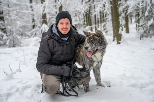 Master with his gray colored Akita Inu dog in the forest during winter with lots of snow, man is smiling and looking at camera while embracing his dog