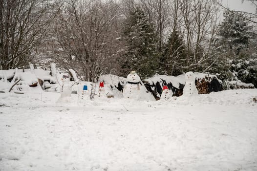 Snow man family in the snow during winter with forest in background