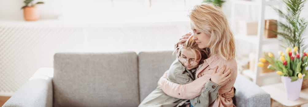 Mother and daughter sitting on the sofa indoor and embracing. Concept of the mother's day, birthday and motherhood.