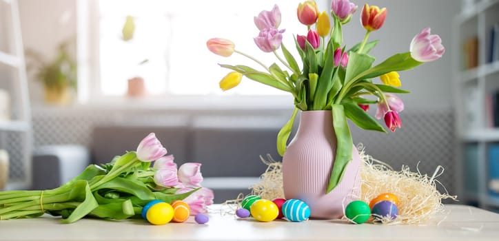 A bunch of tulips in a vase standing on the table and colourful eggs lying on it. Concept of the Easter.