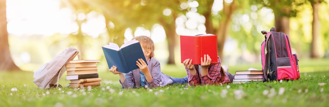 Children lying down on the green field with books in their hands. Concept of the learning, hobby and reading.