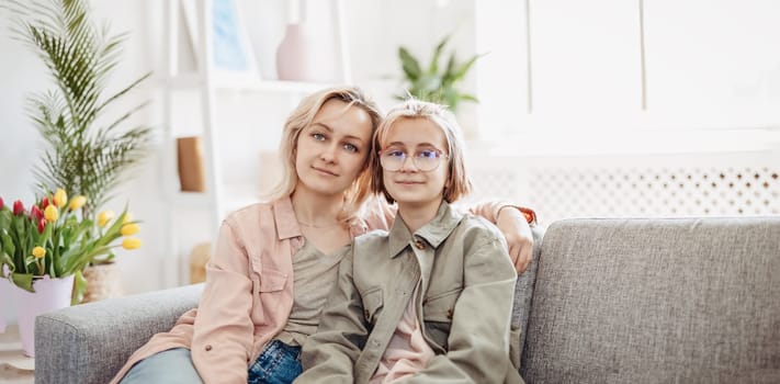 Mother and daughter sitting on the sofa indoor and embracing. Concept of the mother's day and motherhood.