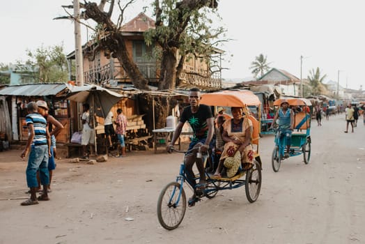 Miandrivazo, Madagascar - November 1. 2022: Traditional rickshaw bicycle with Malagasy passengers on the street, one of the ways to earn money. Everyday life on the cities street of Madagascar.