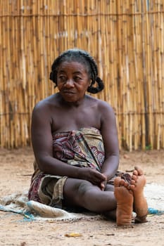 Bekopaka, Madagascar - November 5. 2022: Elder Malagasy woman relaxing in front of hut, there is no job opportunity here. Everyday life on the Madagascar countryside.