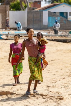 Morondava, Madagascar - November 3. 2022: Malagasy woman with her face painted against the sun and a child in her arms walks along the beach in Morondava.
