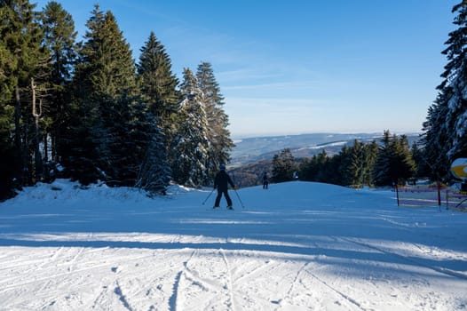 Ski slope on the Wasserkuppe with skiers, snow cannon on the side and with blue sky and trees