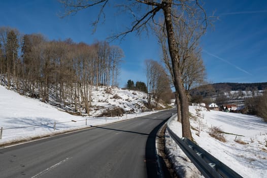 Lonely country road in winter with snow, trees and blue sky, in the High Rhoen, Hesse, Germany