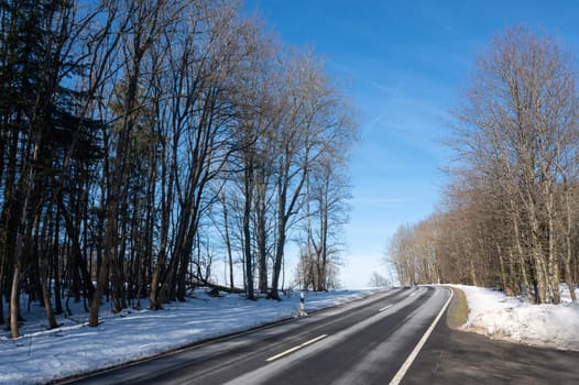 Lonely country road in winter with snow, trees and blue sky, in the High Rhoen, Hesse, Germany