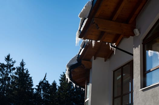 Icicles on a roof with wood and blue sky