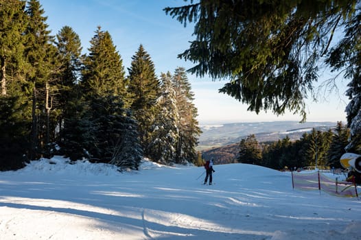 Ski slope on the Wasserkuppe with skiers, snow cannon on the side and with blue sky and trees