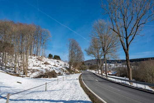 Lonely country road in winter with snow, trees and blue sky, in the High Rhoen, Hesse, Germany