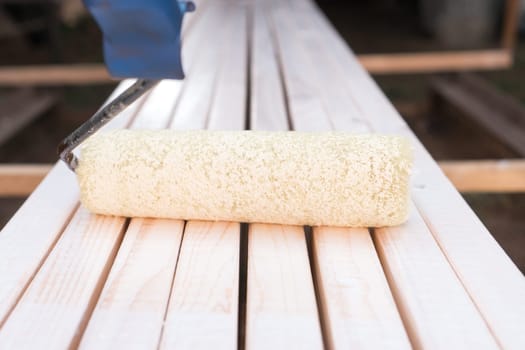 Close up white soft professional paint roller applicator with handle lying on wooden board. Brushing, coloring and making cosmetic repairment. Renewal work, stucco and repair. House remodeling