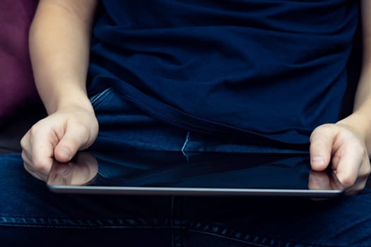 Unrecognizable midsection of male hands holding digital tablet, sit with crossed legs. Elearning, applications and marketplaces online. Remote work and freelance job. Internet streaming and surfing