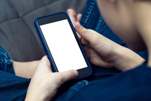 Close up cropped teenage boy using smartphone with white screen in blue mobile case, sitting on sofa. Internet and technology, chatting with friends, social media and smart applications. Copy space