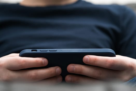 Unrecognizable close up blurred boy hands with smartphone in cover in horizontal orientation. Watching movies and surfing internet online, smart technology and application service. Streaming service
