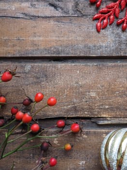 Red fruits of wild rose or rose bush on a wooden background. Golden Christmas ball. Red carved star with sparkles. Autumn, New Year or Christmas still life