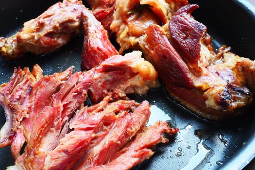 Roasted smoked pork shoulder or knee. Delicious meat on a black baking sheet with drops of vegetable oil, taken out of the oven. Pork delicacy for dinner in a restaurant and family lunch. Red meat.