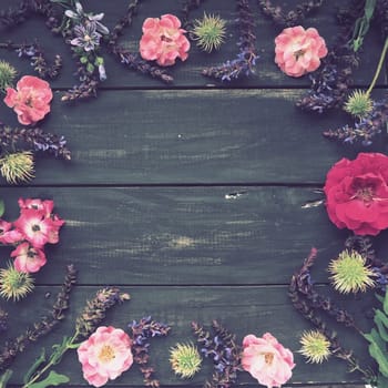 Flowers in a circle on a wooden background. Postcard for the holiday. Roses, geraniums, lavender, sage and hairy chestnuts are placed along the edges on dark boards. Background copy space, flat lay