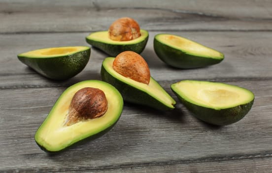 Avocados cut in half, seed visible, on gray wood desk.