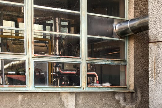 Small old heating plant windows from outside. Heat pipes covered in silver foil visible behind glass.