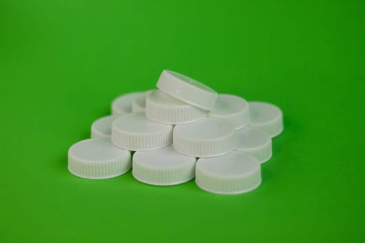 Pyramid of white plastic bottle caps for recycling on a green background. Environmental pollution. Recycling plastic concept