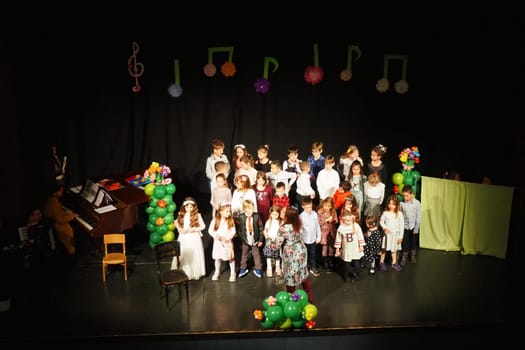 Sremska Mitrovica, Serbia March 8, 2022 Children's choir performance on stage. Children sing. Musical children's group in elegant costumes perform holiday songs for mothers. Dark scene