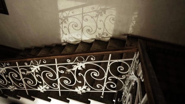 Mysterious staircase with a forged metal railing at night in the dark with dim light. Reflection of curlicues and forging patterns. Railings and steps. Staircase in the museum Sremska Mitrovica Serbia