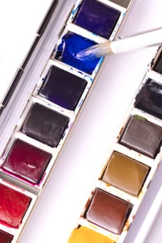Paint brush dipping into blue pan of watercolor in tin.