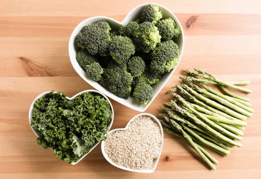 Flat lay of healty fresh broccoli kale brown rice and asparagus, some in heart shaped bowls