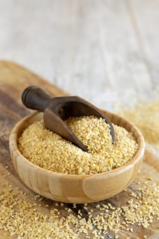 Raw Dry bulgur wheat grain in a wooden bowl with a scoop close up, copy space. Vegetarian and Vegan, Mediterranean and Middle Eastern cuisine. Healthy lifestyle
