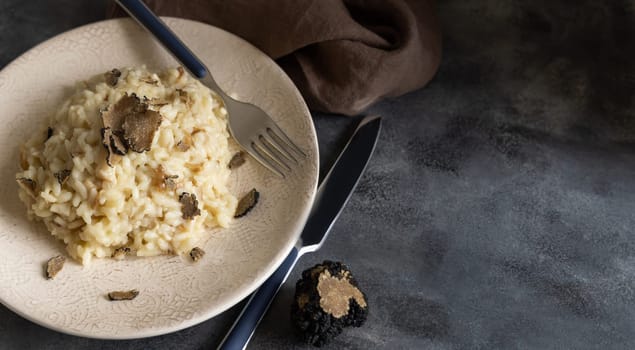 Risotto with wild porcini mushrooms and black truffles from Italy served in a plate close up on grey table, copy space. Eating Italian gourmet cousine