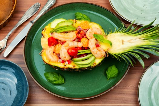 Half a pineapple with vegetables, rice and seafood on a white plate. Salad