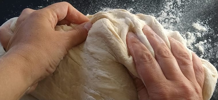 Hands knead the dough. The woman kneaded dough for baking or dumplings. Preparation of flour, water and egg mass for thermal processing. Chef hands.