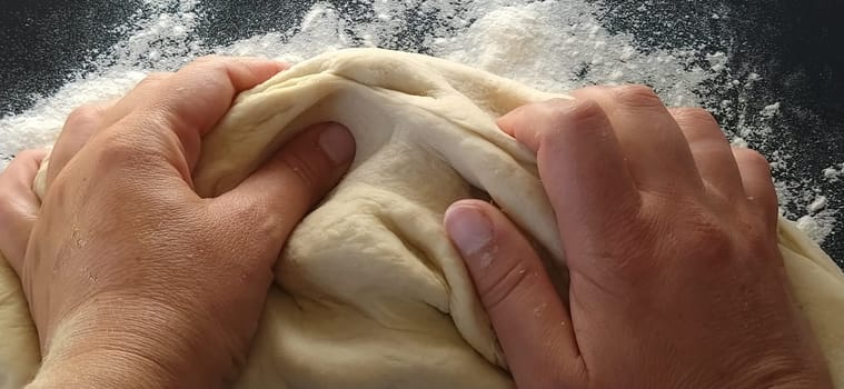 Hands knead the dough. The woman kneaded dough for baking or dumplings. Preparation of flour, water and egg mass for thermal processing. Chef hands.