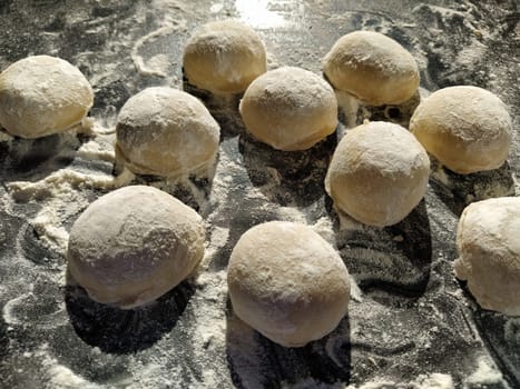 Round pieces of shortbread dough for making cookies or gingerbread. Raw buns or dumplings with scattered flour around on black background.
