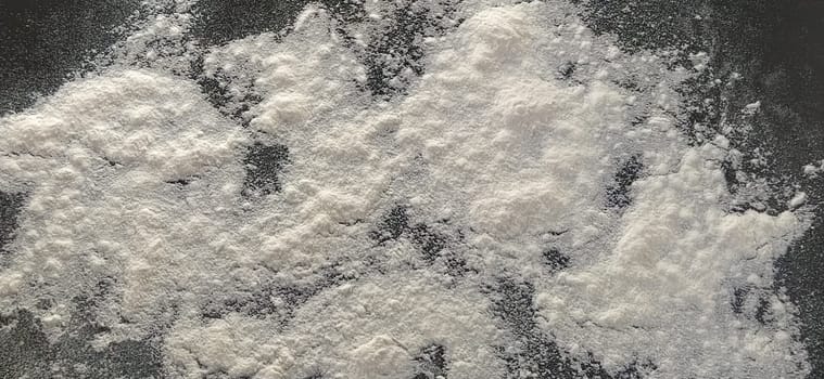 White wheat flour, sifted and sprinkled on a black background. Preparation for baking. Close up and selective focus.