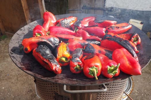 Roasting red peppers for a smoky flavor and quick peeling. Thermal processing of the pepper crop on metal circle. Brazier container used to burn charcoal fuel for cooking, heating or cultural rituals
