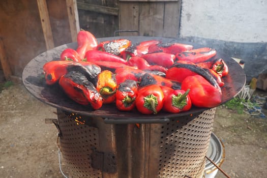 Roasting red peppers for a smoky flavor and quick peeling. Thermal processing of the pepper crop on metal circle. Brazier container used to burn charcoal fuel for cooking, heating or cultural rituals