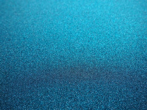 Deep blue. Texture of rough paper or cardboard. Defocused bokeh sparkles and shining. Festive blue background with illuminated sapphire gradient.