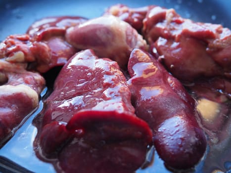chicken liver, kidney and heart in a non-stick skillet. The offal of the bird is placed in a dark bowl and sprinkled with vegetable oil. Cooking food high in heme iron. Anti-anemic diet.