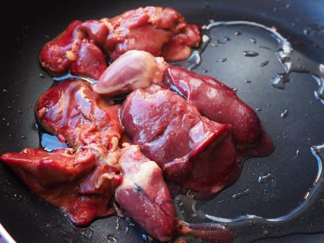 chicken liver, kidney and heart in a non-stick skillet. The offal of the bird is placed in a dark bowl and sprinkled with vegetable oil. Cooking food high in heme iron. Anti-anemic diet.