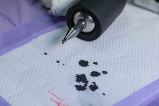 A tattoo machine sitting on the work table after finishing a tattoo, with black ink splattered under it.